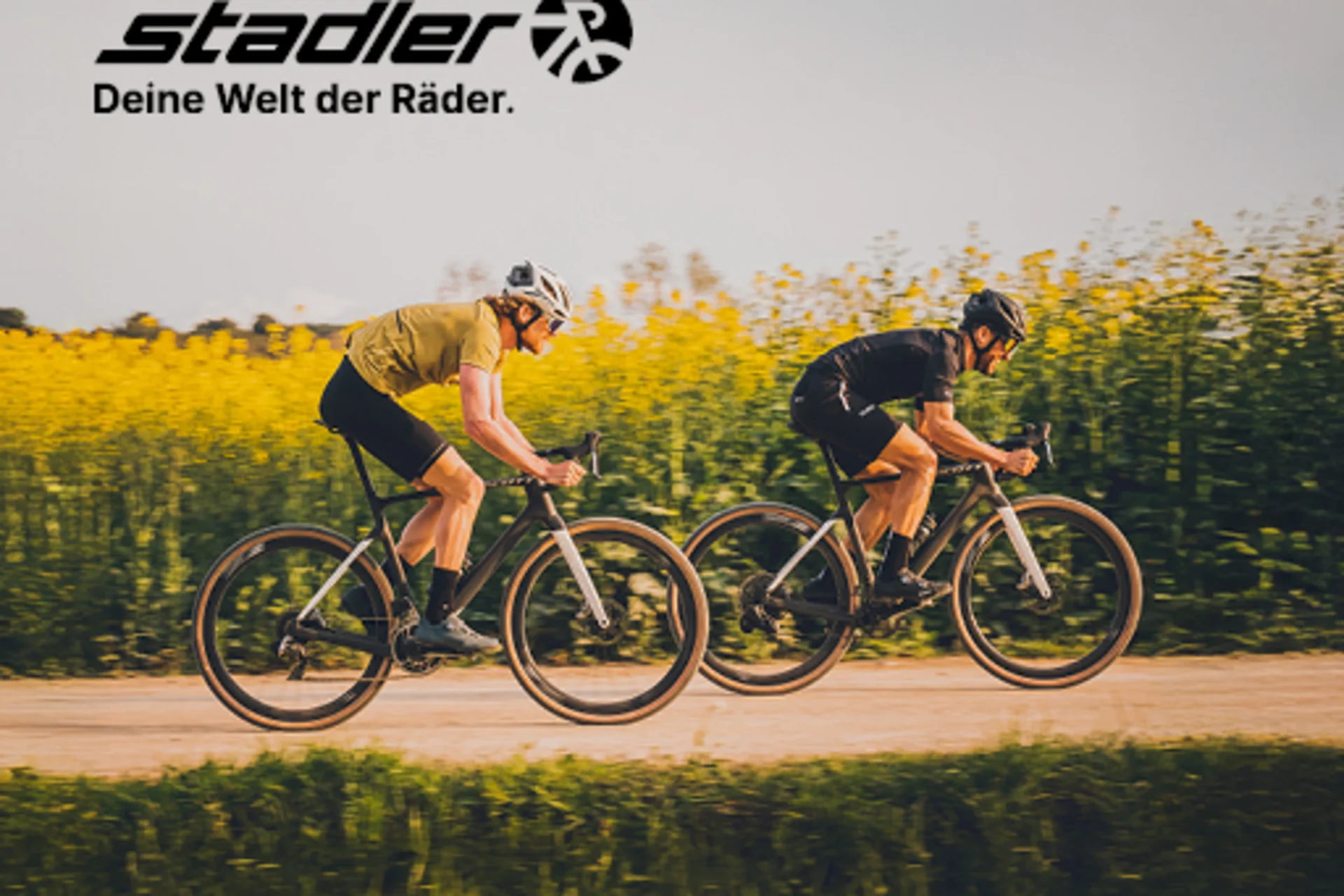 Gravelbike Holidays © Scott by JAF Zwei Radfahrer fahren auf einem Weg vor einem Feld mit gelben Blumen