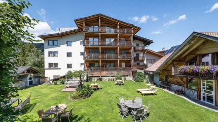 Sporthotel Exclusive © Sporthotel Exclusive SAS Großer Garten mit Tischen, Stühlen und Liegestühlen vor Alpenhaus