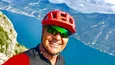 Gravelbike Holidays © Andrea Maino Mann mit rotem Fahrradhelm macht Selfie vor Berg und See