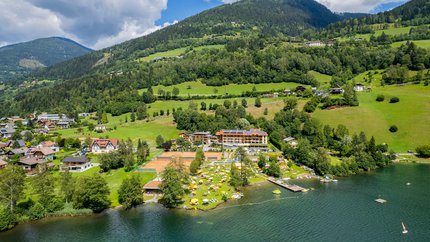 Familien- & Sportresort Brennseehof © Gert Perauer Seeufer mit Strand, Liegestühlen und Tennisplätzen vor bewaldeten Bergen