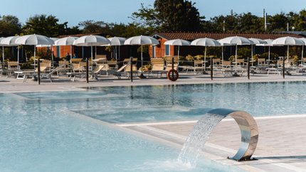 Natural Village Resort © Luigi Ventimiglia Moderner Pool mit Wasserfontäne und Liegestühlen unter weißen Sonnenschirmen