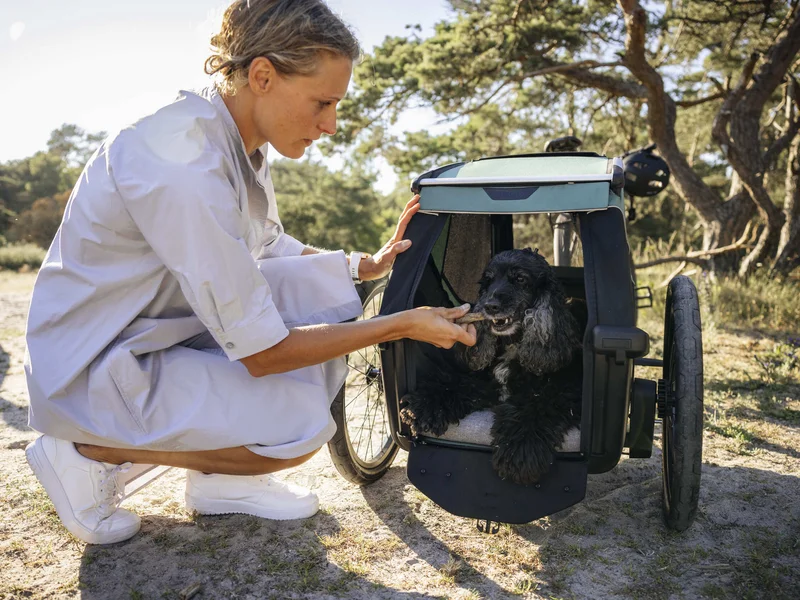 Gravelbike Holidays © Thule Eine Frau gibt einem Hund in einem Fahrradanhänger ein Leckerli