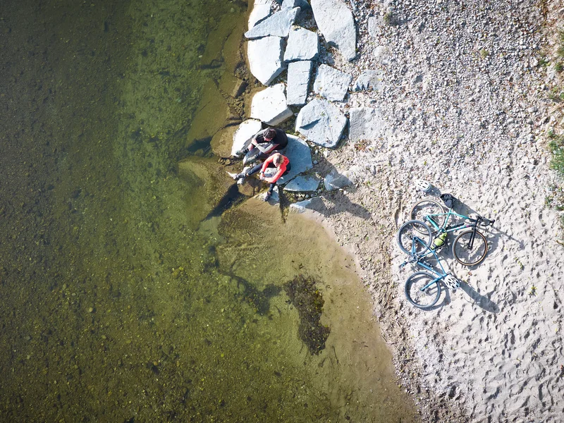 Gravelbike Holidays © Oberbayern.de - Tobias Köhler Zwei Radfahrer sitzen am Ufer neben zwei Fahrrädern