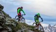Gravelbike Holidays © Markus Greber Zwei Mountainbiker fahren an einem steilen Berg mit schneebedeckten Gipfeln im Hintergrund