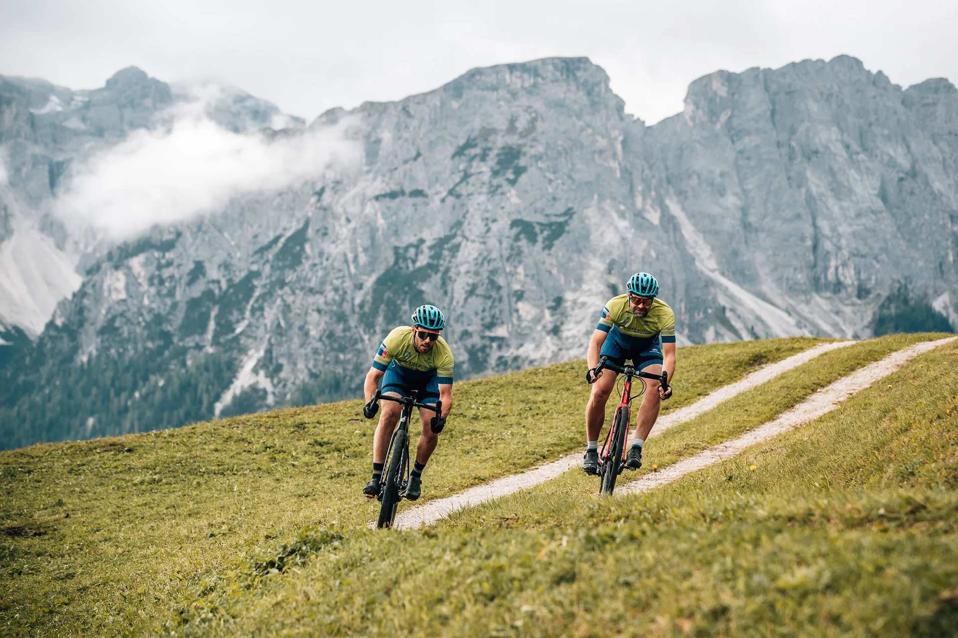 Gravelbike Holidays © Jens Scheibe Zwei Radfahrer fahren auf einem hügeligen Weg mit Bergen im Hintergrund
