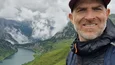 Gravelbike Holidays © Toni Unterkofler Mann mit Rucksack vor Berglandschaft und See bei Nebel