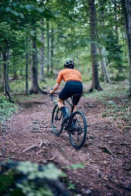 Gravelbike Holidays © Tobias Köhler Radfahrer in orange Trikot fährt im Wald auf einem unbefestigten Weg