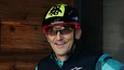 Gravelbike Holidays © Ziga Intihar Mann mit Fahrradhelm zeigt Daumen hoch vor beleuchtetem G an Holzwand