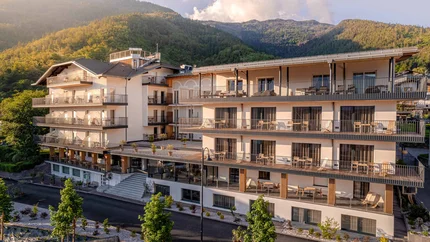Cristallo Sport & Wellness Hotel © Andrea Acler Modernes Hotelgebäude vor bewaldeten Bergen im Sonnenlicht