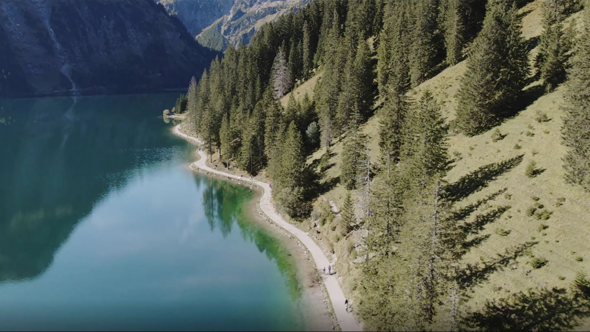 Gravelbike Holidays © Andreas Vigl Wanderweg entlang eines klaren Bergsees mit Nadelbäumen und Bergen