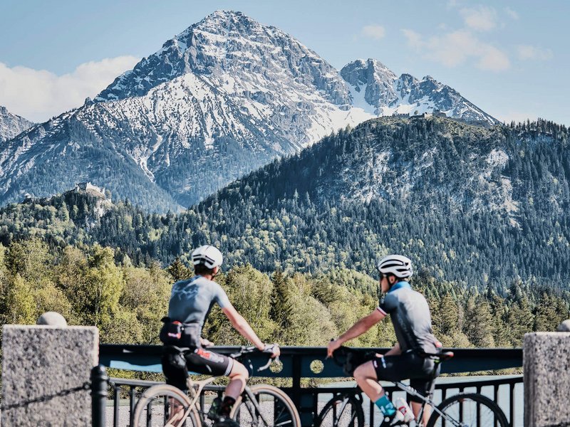 Gravelbike Holidays © Dominik Somweber Zwei Radfahrer blickend auf schneebedeckten Berg und bewaldete Hügel
