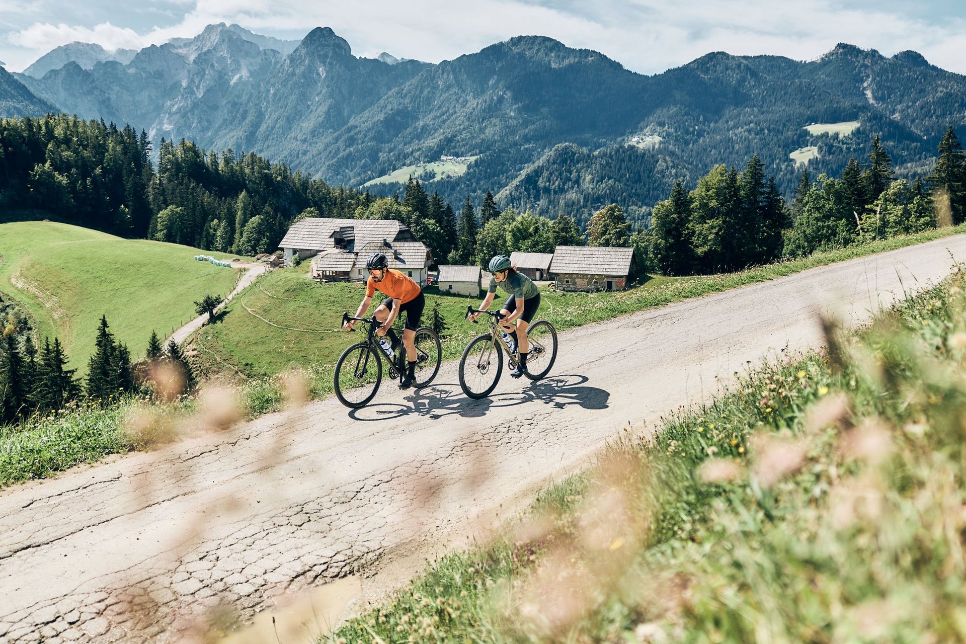 Gravelbike Holidays © Tobias Köhler Zwei Radfahrer fahren bergauf auf einer Straße in den Bergen bei Sonnenschein