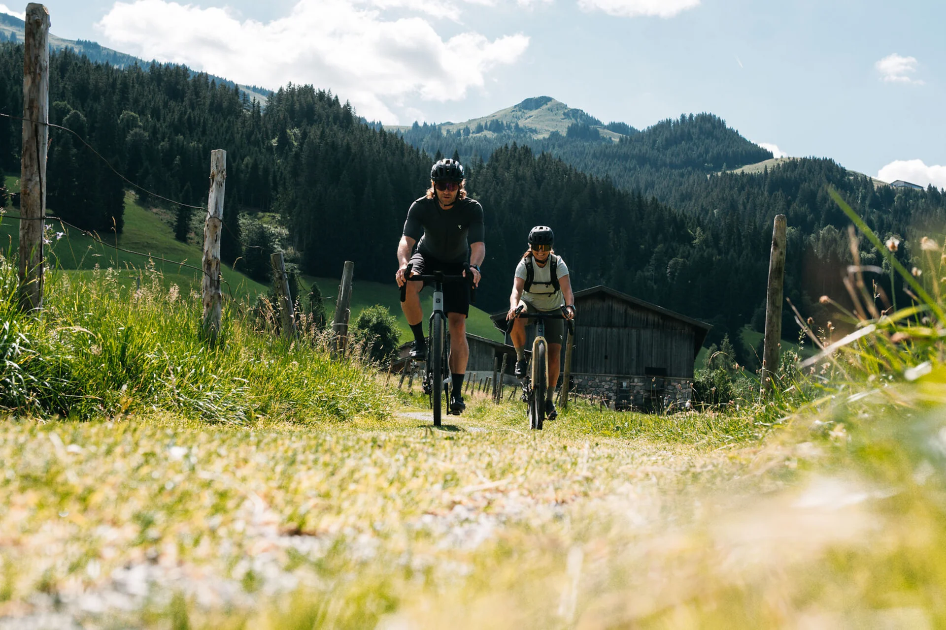 Gravelbike Holidays © Martina Wunderle / Flo Distl Zwei Radfahrer fahren auf einem Weg in den Bergen bei sonnigem Wetter